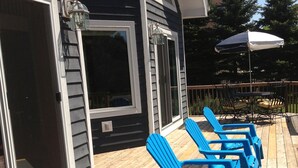 A deck with blue Adirondack chairs and a table, a sliding glass door, and a white umbrella. - Exceptional Chalet near Harbor, Nubs Nob and Boyne Highlands Ski and Golf Resort (Harbor Springs)