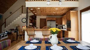 A dining area with a wooden table set for four, a kitchen in the background, and a staircase leading to an upper level. - Exceptional Chalet near Harbor, Nubs Nob and Boyne Highlands Ski and Golf Resort (Harbor Springs)