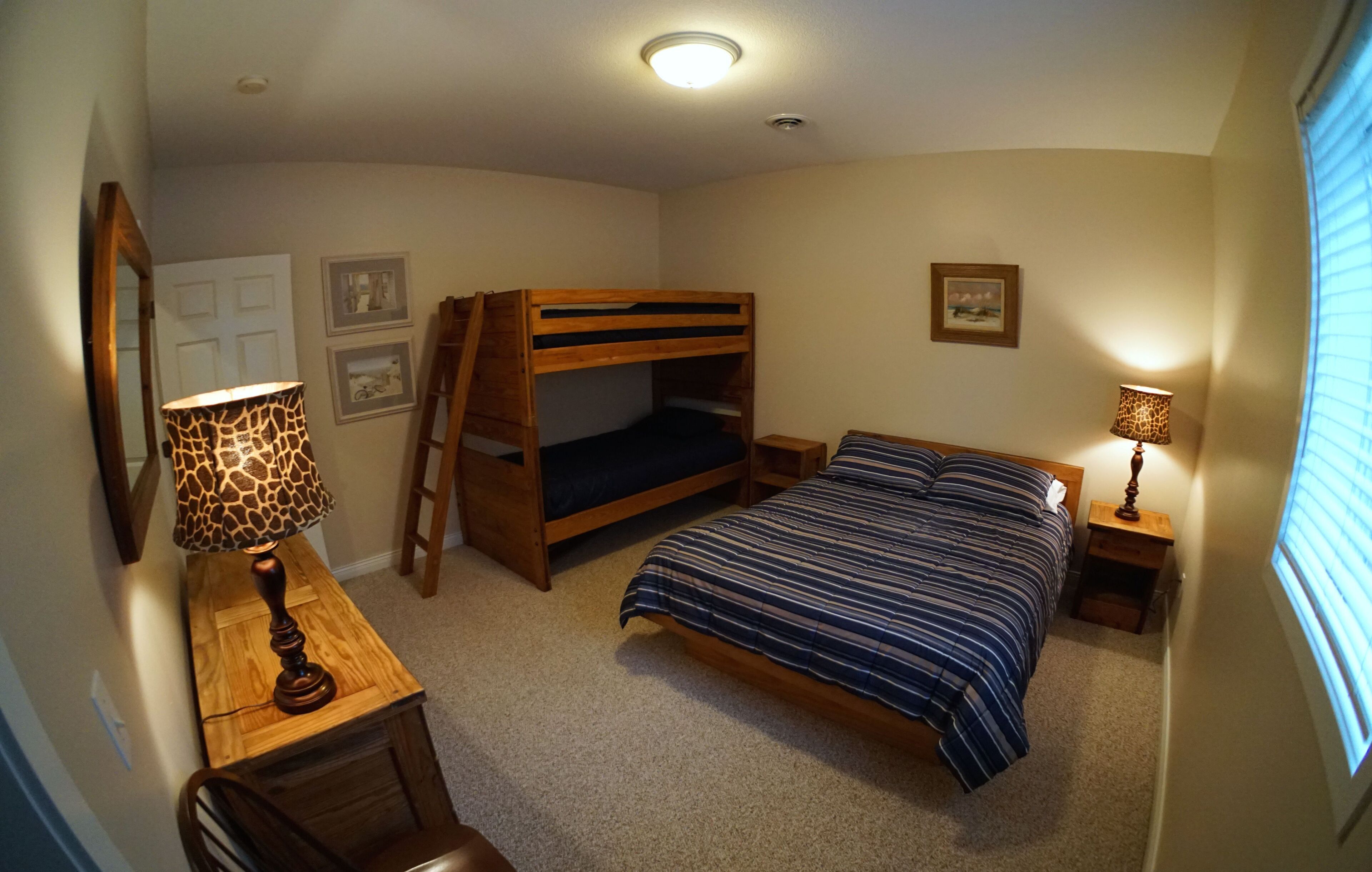 Une chambre avec un lit superposé, un bureau avec une lampe et une fenêtre avec des stores.