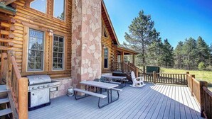 A wooden cabin with a stone chimney, outdoor grill, picnic tables, and a deck overlooking a forested area. - Huge Log Cabin on 20 Acre Ranch close to Grand Canyon with Spectacular Views! (Williams)