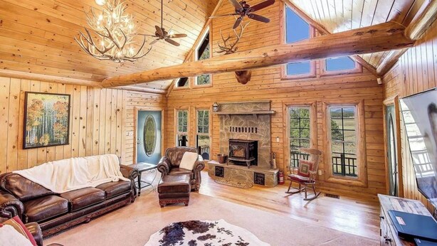 A log cabin interior with a fireplace, leather sofa, and a chandelier. - Huge Log Cabin on 20 Acre Ranch close to Grand Canyon with Spectacular Views! (Williams)