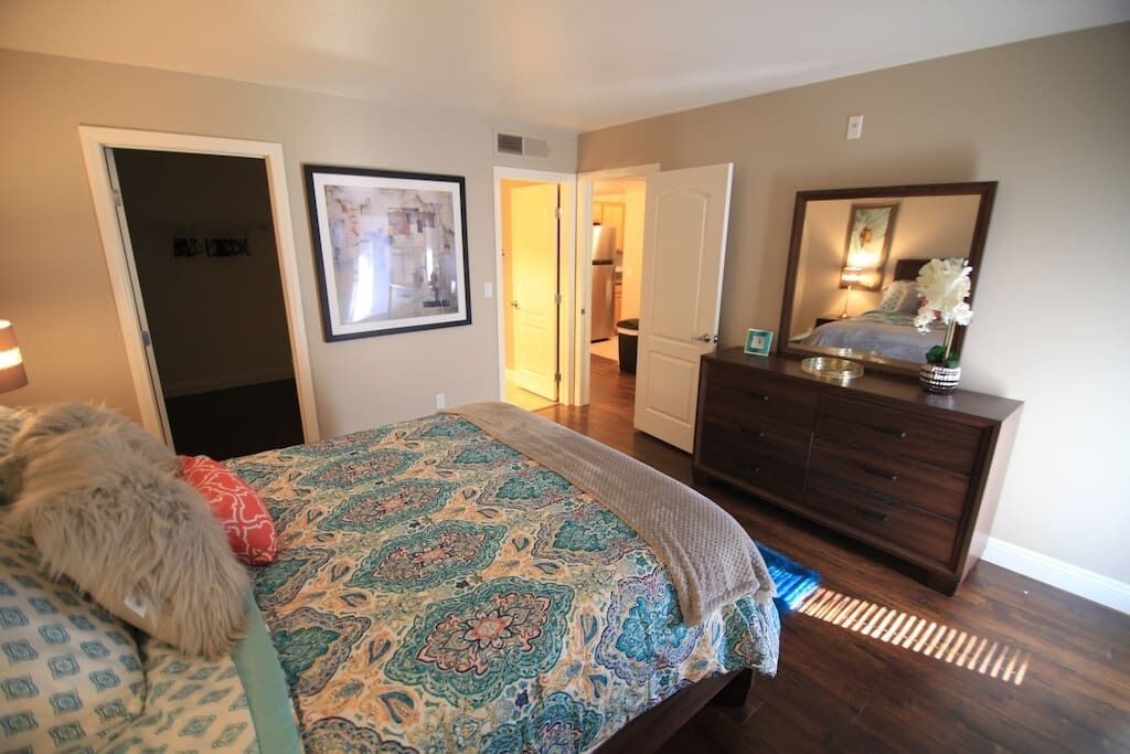 A bedroom with a bed, dresser, and a door leading to another room.