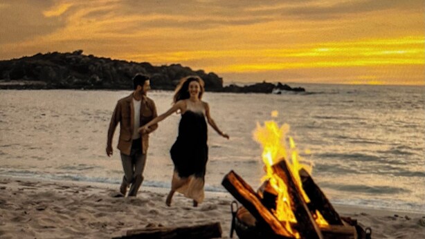 A beach scene with a campfire and two people walking.