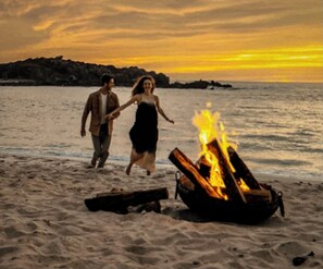 A beach scene with a campfire and two people walking.
