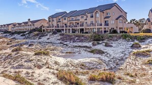 A row of modern multi-story buildings with balconies, situated on a sandy terrain with sparse vegetation.