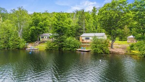 A lakeside cabin with a dock and chairs, surrounded by lush greenery.