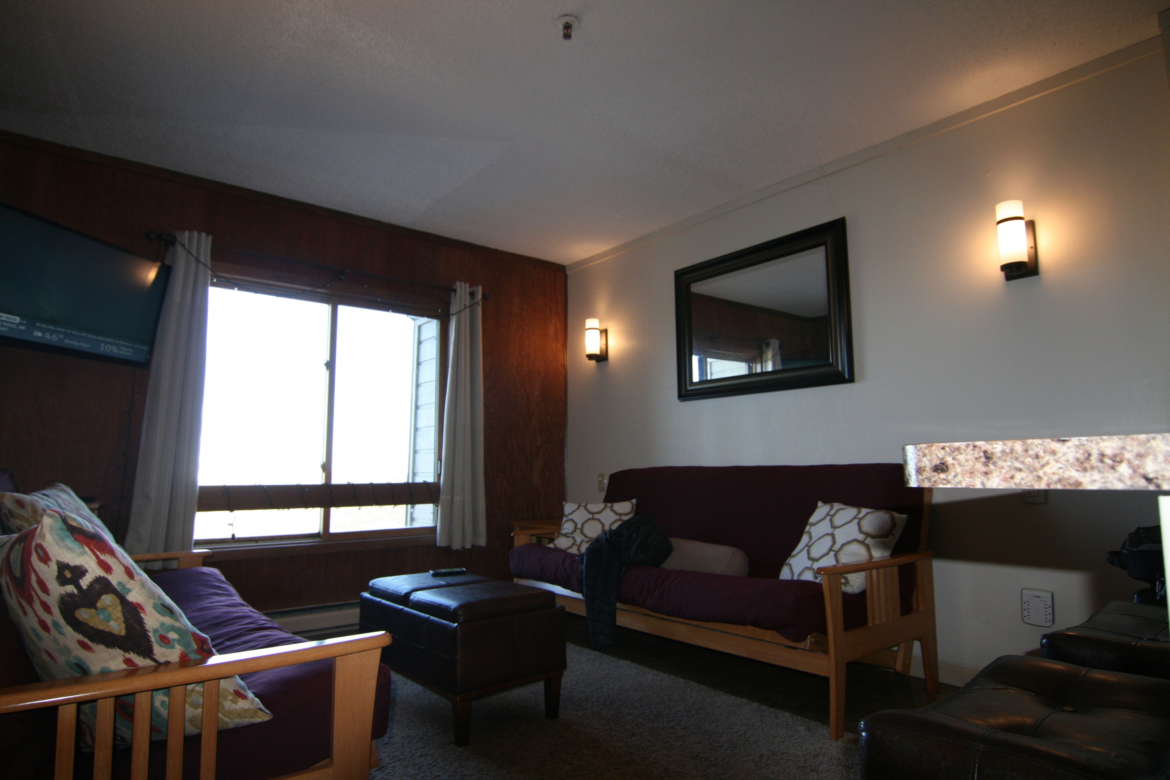 A room with a bed, a sofa, a chair, and a window with curtains.