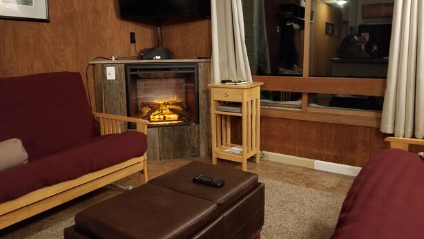 Ein Wohnzimmer mit Kamin, Wandfernseher und großem Fenster mit Vorhängen.