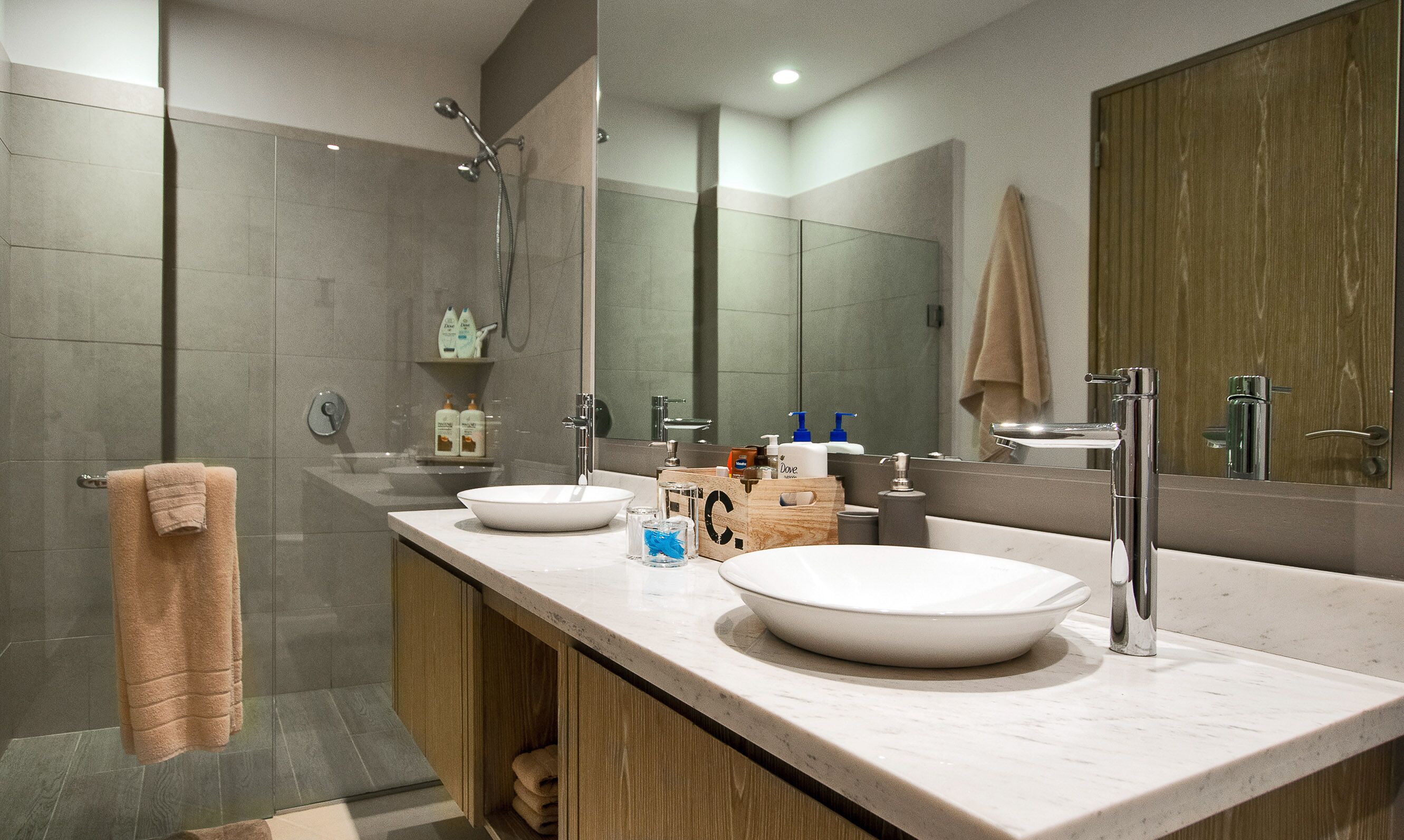 A modern bathroom with a large mirror, two sinks, a shower, and a towel rack.