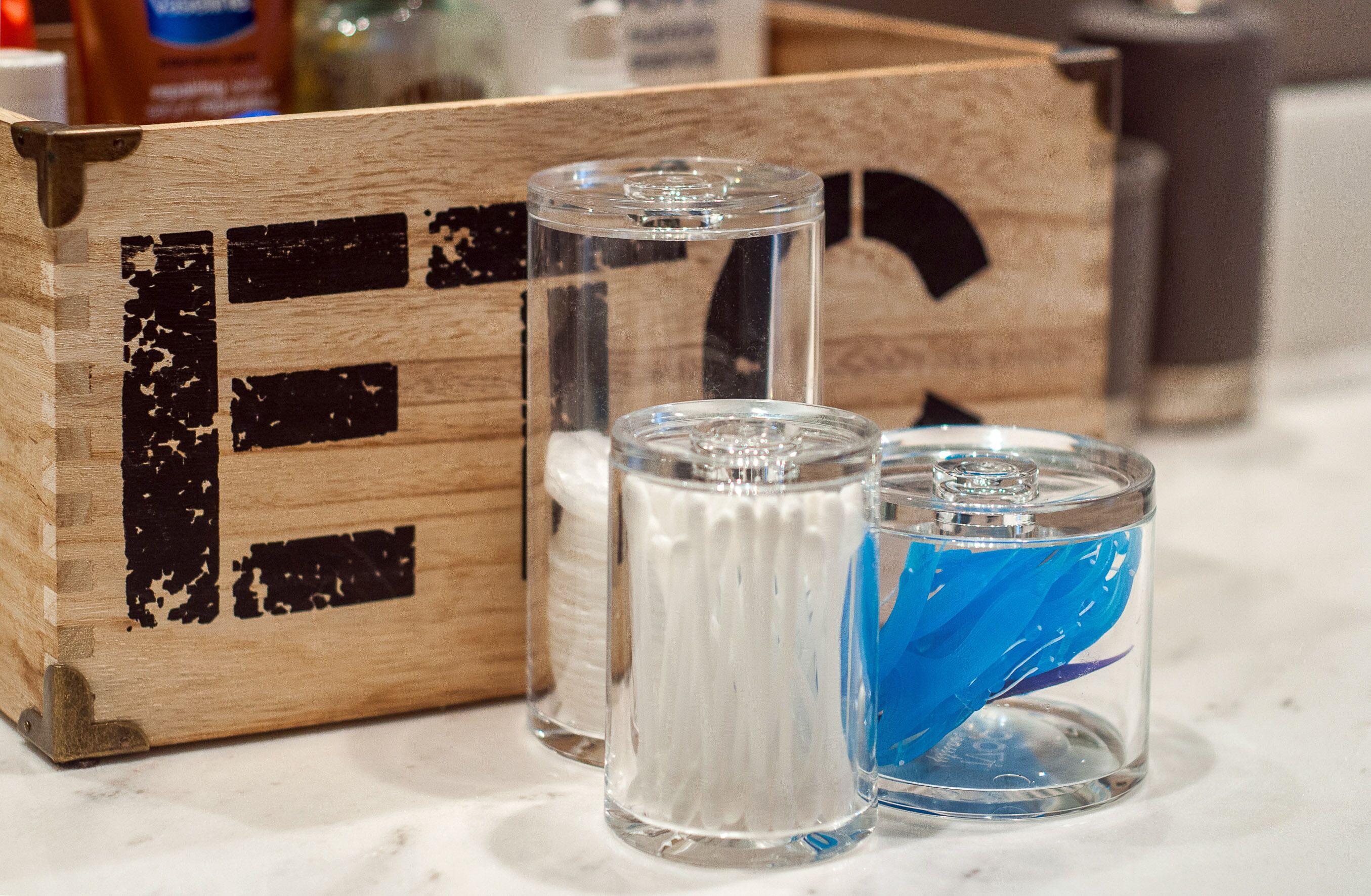 Una caja de madera con tres recipientes de vidrio, uno con un contenido blanco y otro con objetos azules en su interior.