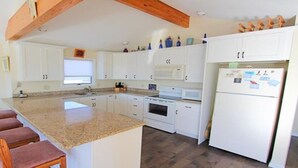 Una cocina con armarios blancos, encimera de granito, horno empotrado y refrigerador.