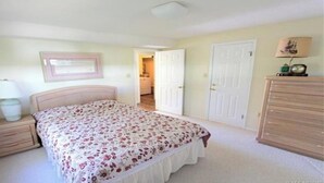 Un dormitorio con cama, mesitas de noche, cómoda y una puerta que da a otra habitación.