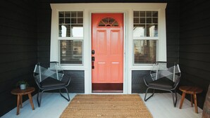 A porch with a red door, two black chairs, and a woven mat.