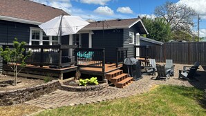 A residential house with a covered patio, a wooden deck, and a brick pathway.