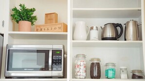 A kitchen with a microwave, a potted plant, and various jars of food on the shelves.