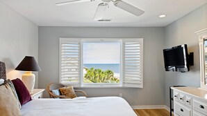 Ein Schlafzimmer mit Bett, Nachttisch, Lampe, Sessel, Kommode, Fernseher und einem Fenster mit Rollläden.