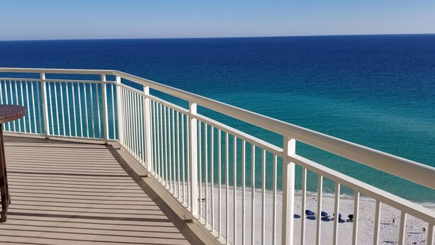 Una terraza con barandilla que da a una playa con agua azul cristalina.