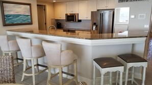 Una cocina moderna con armarios blancos, electrodomésticos de acero inoxidable y una isla central con taburetes.
