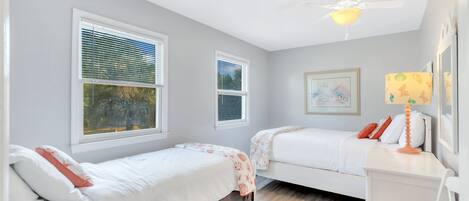 A bedroom with two single beds, a ceiling fan, and a window with blinds.