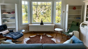 Een kamer met een grote erker, een bureau, een leren bank, een groene fauteuil en een vachttapijt.
