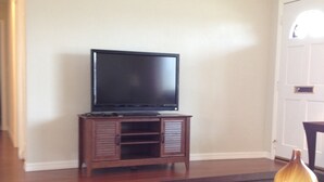 A living room with a flat-screen TV on a wooden stand, a dining table with a vase, and a striped rug. - No snow here. 5 minute walk to the beach. Quiet neighborhood. (Ormond Beach)
