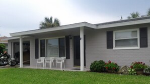 A single-story house with a covered porch, a garage, and a small garden with potted plants. - No snow here. 5 minute walk to the beach. Quiet neighborhood. (Ormond Beach)