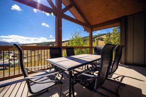 Un espacio al aire libre techado con una mesa y sillas, con vistas a un paisaje montañoso.