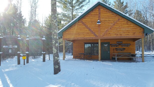 A wooden cabin with a green roof, a signboard, and a picnic table.