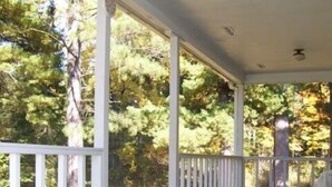 A covered porch with white railings and a wooden floor, surrounded by trees.