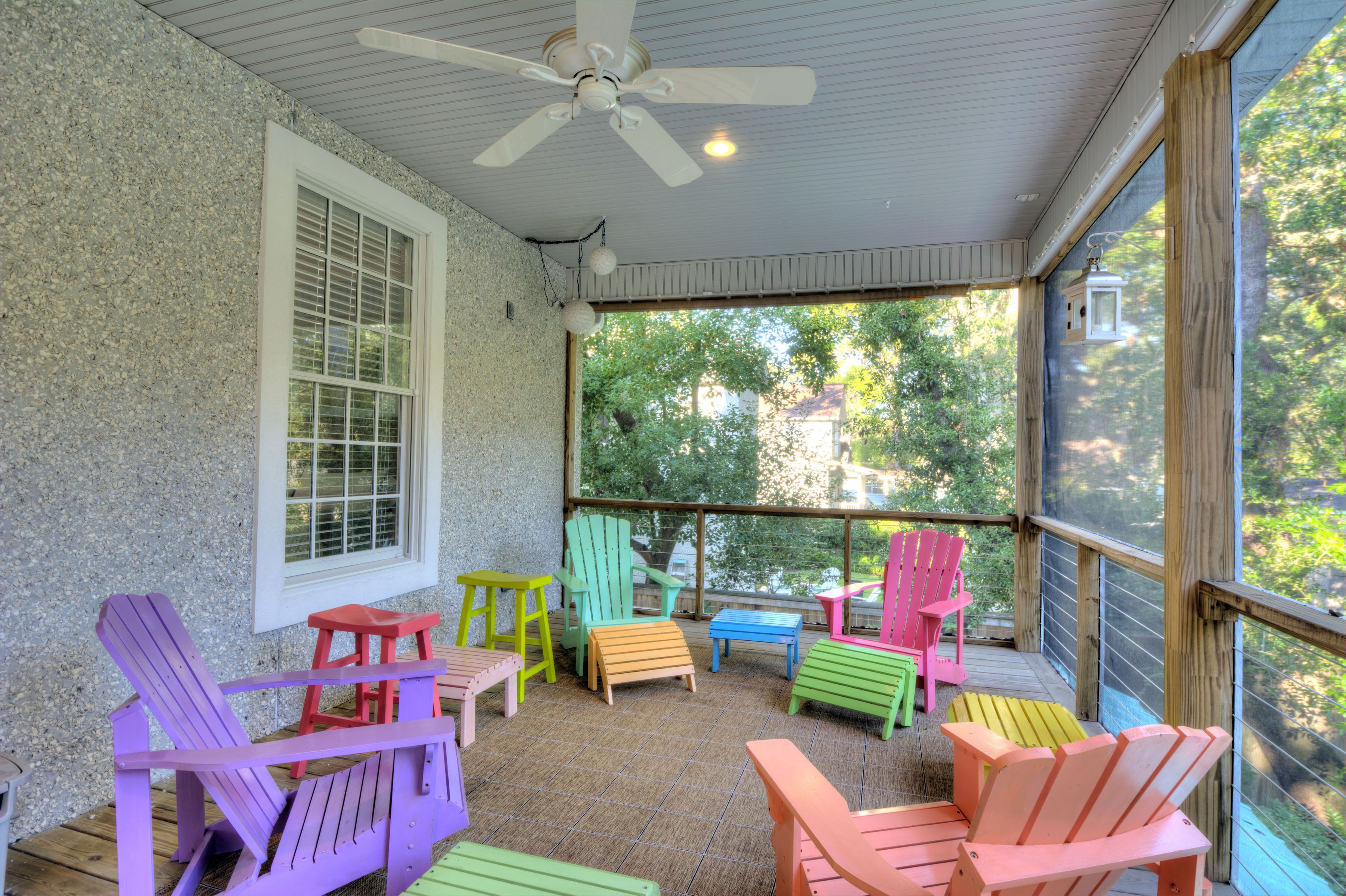 A covered outdoor seating area with colorful Adirondack chairs and a ceiling fan.