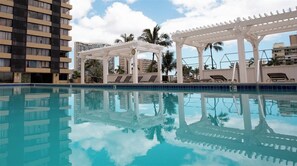 A swimming pool with a white pergola and lounge chairs, surrounded by tall buildings and palm trees. - Waikiki Hotel Studio @ Hawaiian Monarch Building 1 day min (Honolulu)