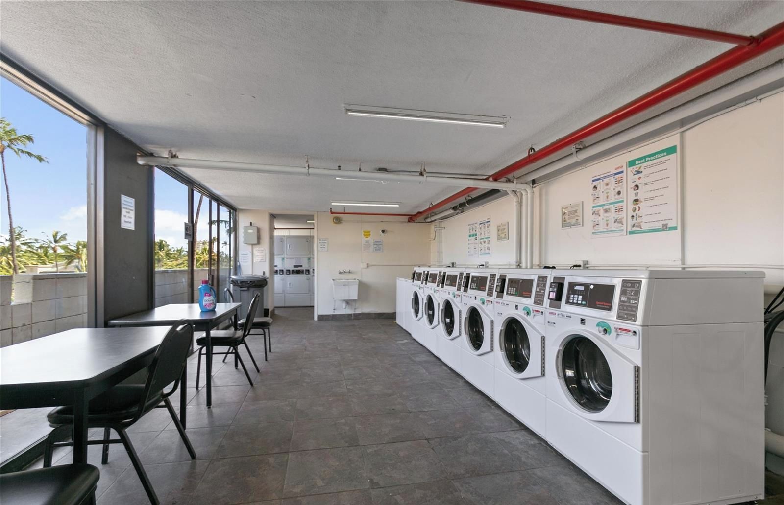 A laundromat with multiple washing machines, a table with chairs, and a view of the outdoors.