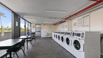 A laundromat with multiple washing machines, a table with chairs, and a view of the outdoors.