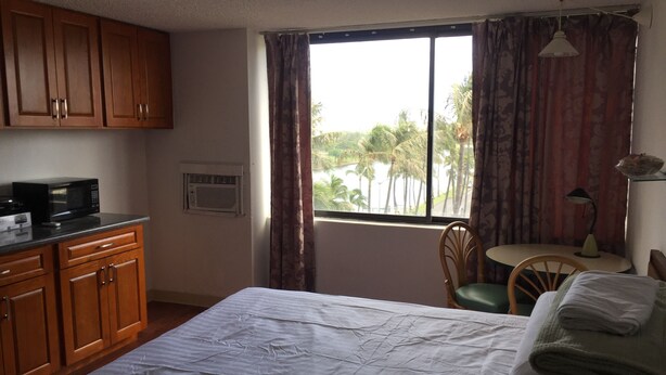 Una habitación de hotel con cama, escritorio y silla, armarios de madera, microondas y ventana con cortinas.