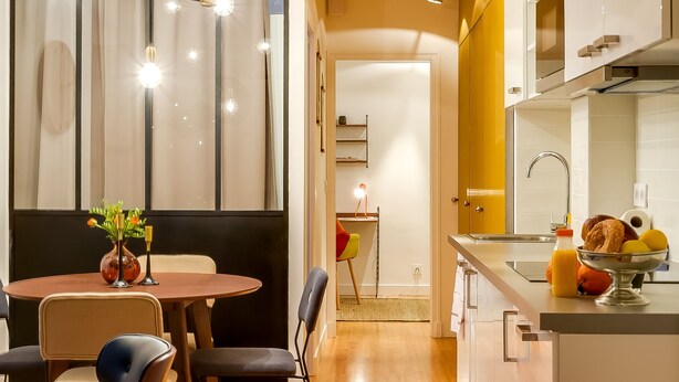 Eine moderne Küche mit Holzboden, einem Essbereich mit rundem Tisch und Stühlen sowie einer Küchenarbeitsplatte mit Spüle und Obstschale.