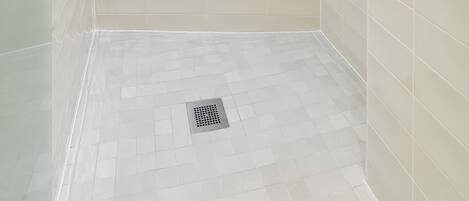A modern shower with a handheld showerhead and a fixed showerhead, tiled walls, and a visible drain.