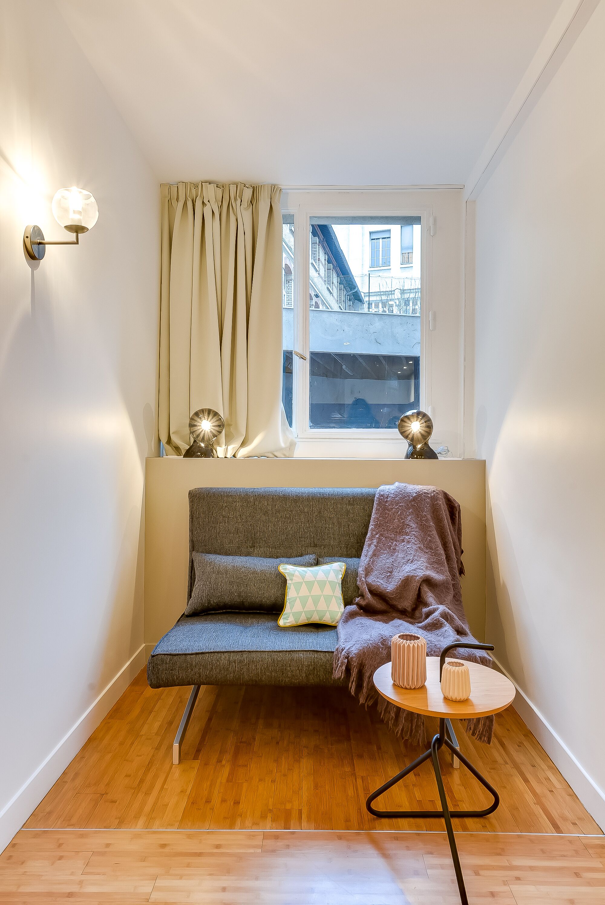 A cozy room with a sofa, a small round table, and a window with curtains.