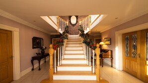 A grand staircase with a wooden finish, flanked by white railings and decorated with festive garlands.