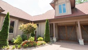 A two-story house with a covered driveway, a garage, and a landscaped front yard with various shrubs and a tree.