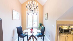 A dining area with a glass table and chairs, a chandelier, and a window with natural light.
