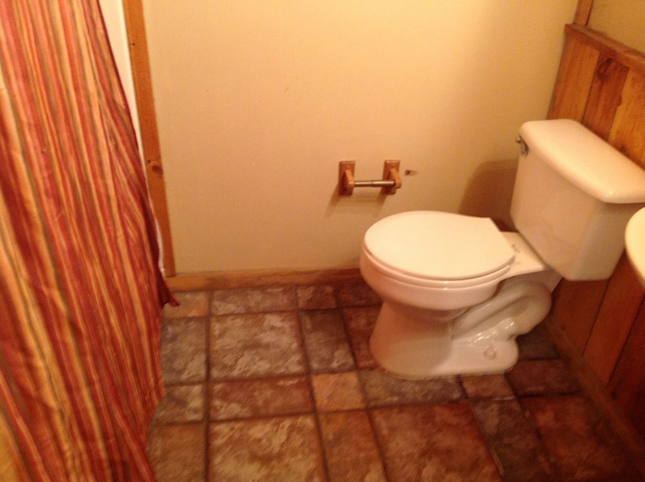 Een kleine badkamer met een wit toilet, een houten kastje en een douchegordijn met strepen.