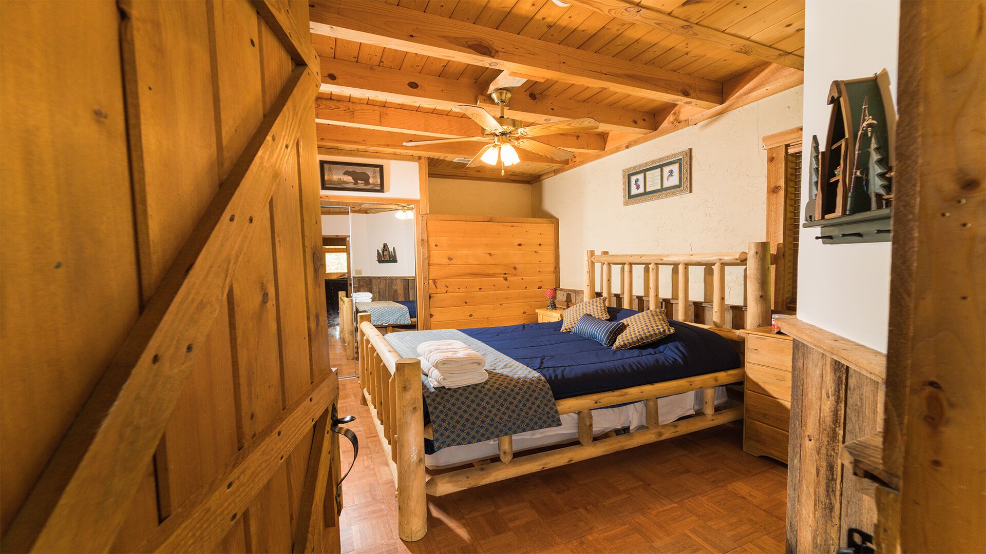A wooden cabin-style bedroom with a bed, wooden headboard, and a ceiling fan.