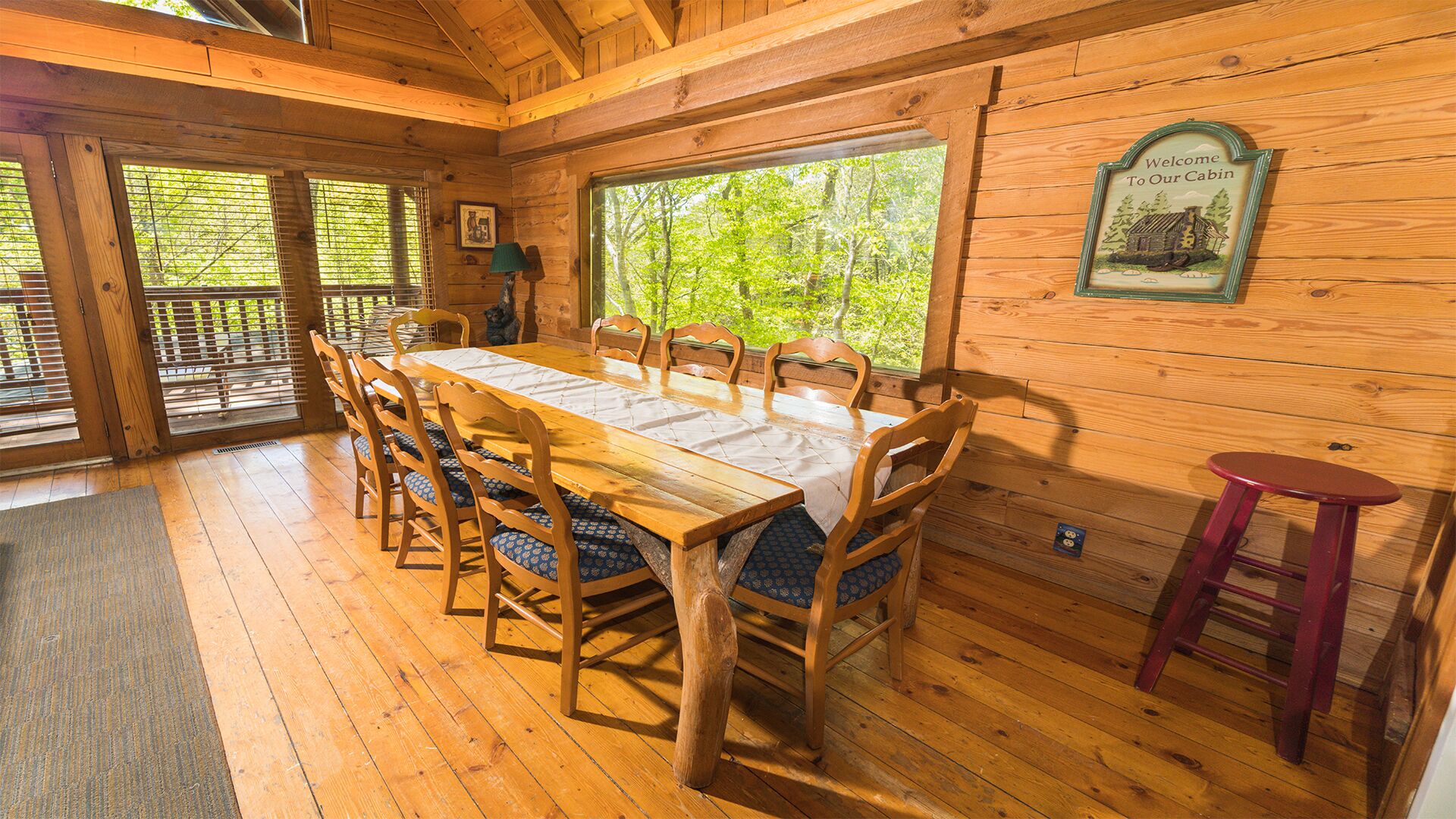 A wooden cabin interior with a dining table, chairs, a bench, and a welcome sign.