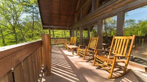 Une terrasse en bois avec des fauteuils à bascule et un banc, donnant sur une zone boisée.
