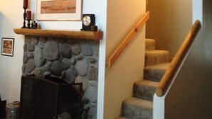 A staircase with a stone fireplace, a clock, and a framed picture on the landing. - Pet Friendly Circle 4 Cabin And People Friendly As Well (Sunriver)