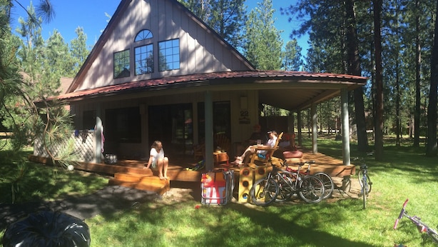 A house with a porch, a bicycle, and a person sitting on the porch. - Pet Friendly Circle 4 Cabin And People Friendly As Well (Sunriver)