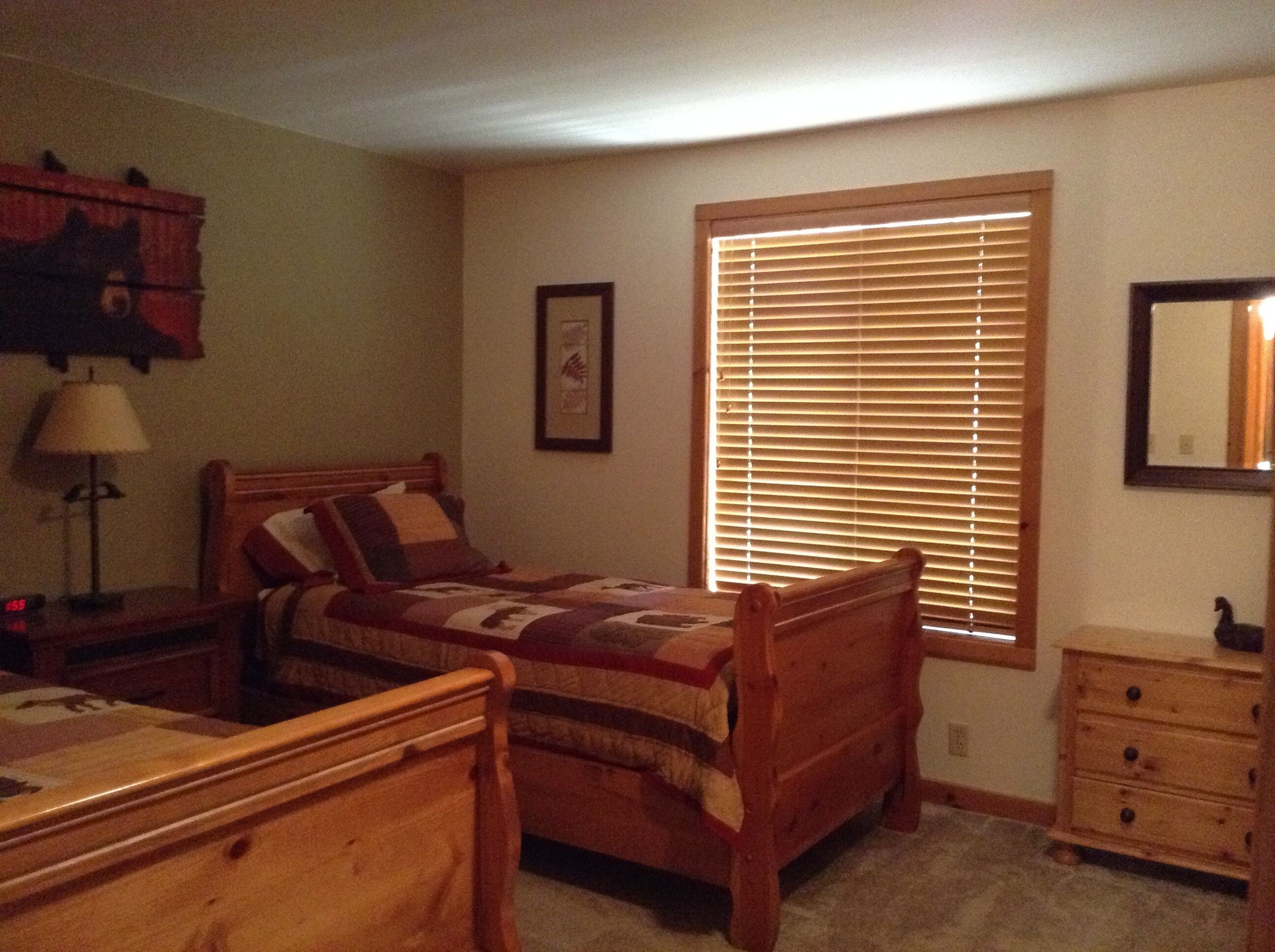 Un dormitorio con cama de madera, una mesita de noche, un aparador, una ventana con persianas y un cuadro en la pared.