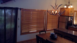 A dining area with a wooden table and chairs, a chandelier with antlers, and a kitchen with wooden cabinets and a refrigerator. - Pet Friendly Circle 4 Cabin And People Friendly As Well (Sunriver)