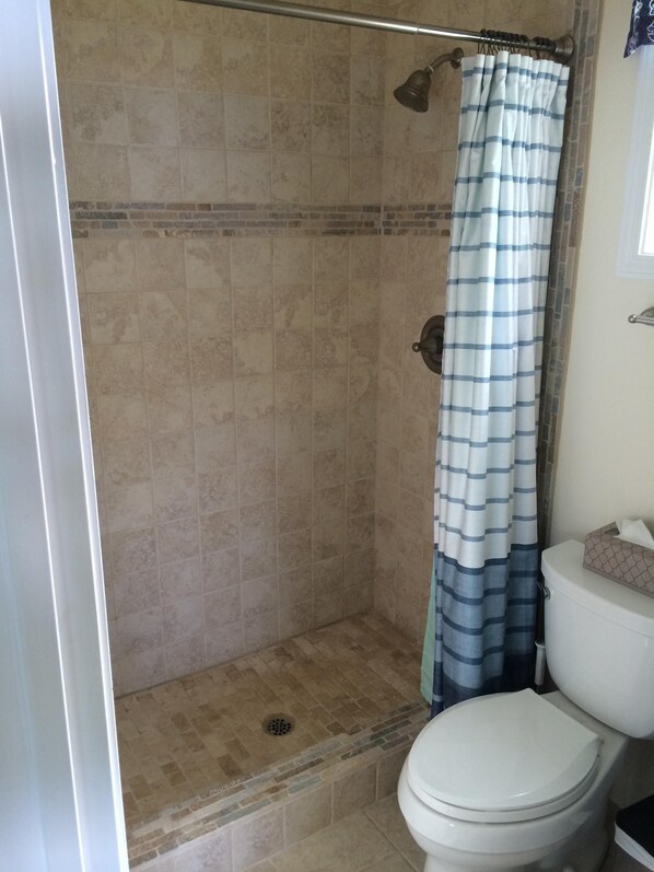 A bathroom with a shower, tiled walls, a toilet, and a curtain.