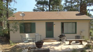 Una cabaña de madera de un piso con un patio, mobiliario exterior y una parrilla.